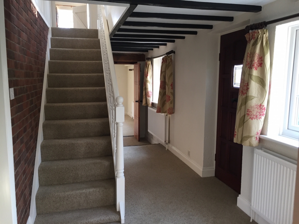 Dated looking hallway with beige carpet and short curtains